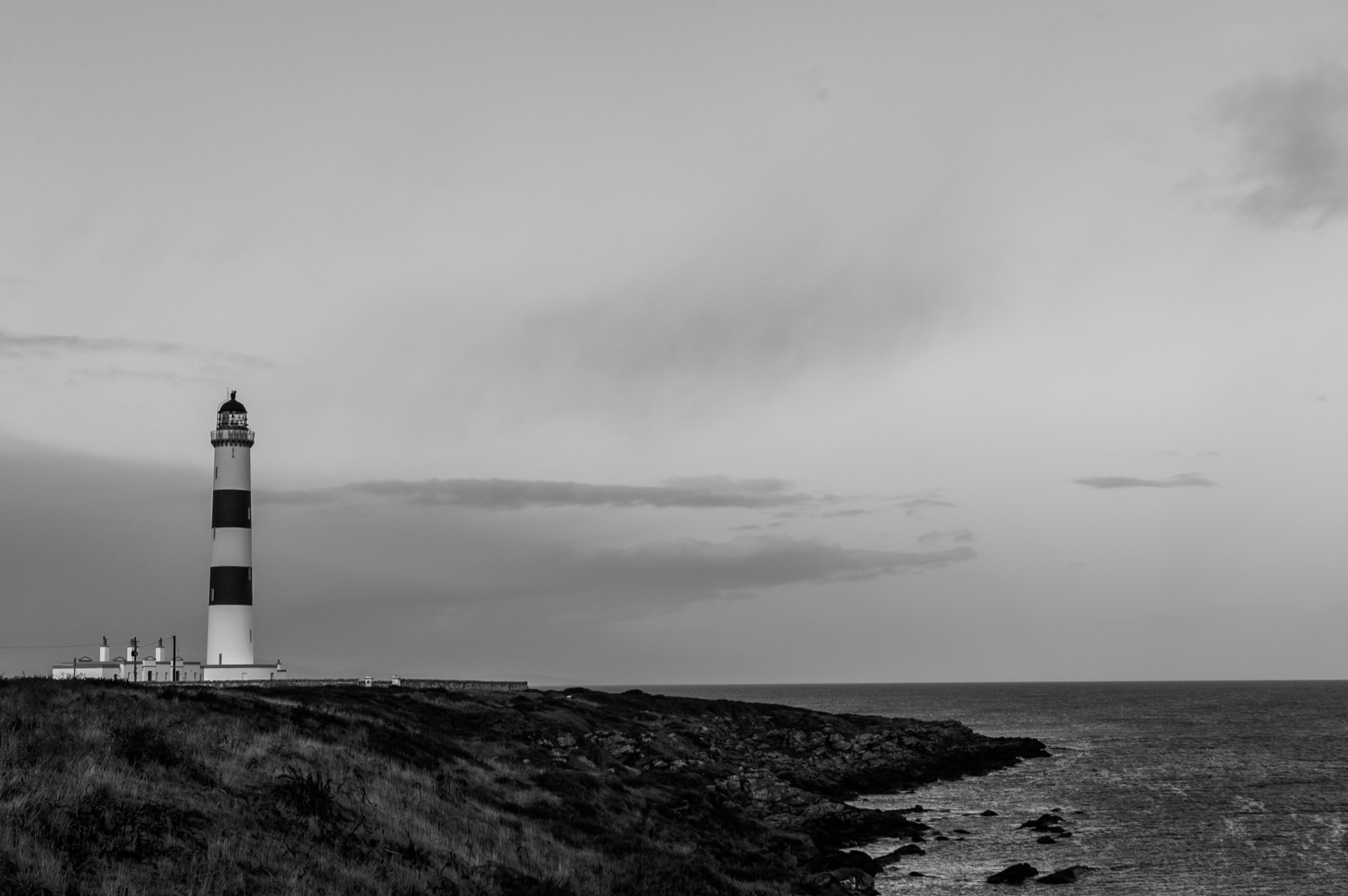 A black-and-white lighthouse standing over a rocky coastal headland